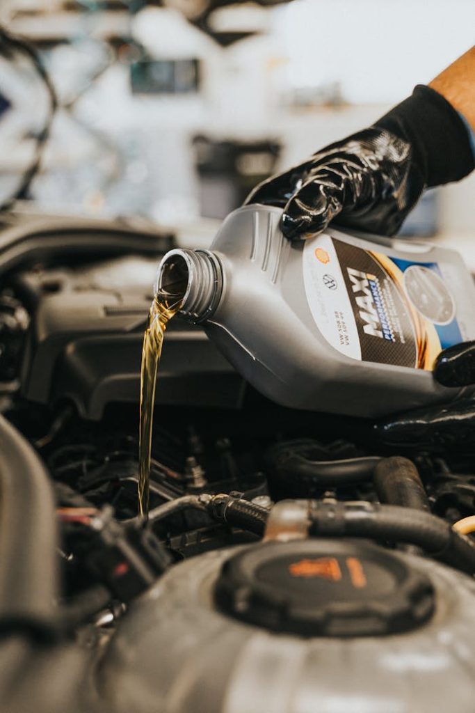 Close-up of a mechanics gloved hand pouring engine oil into a vehicle.